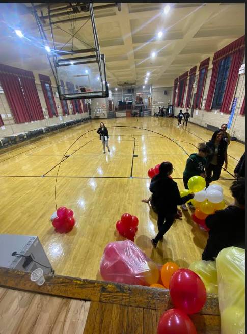 Stage view of students setting up Fall colored balloons in empty gymnasium before Thanksgiving potluck