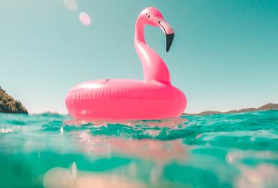Pink flamingo flotation device floating on beach water on a sunny day with clear blue sky