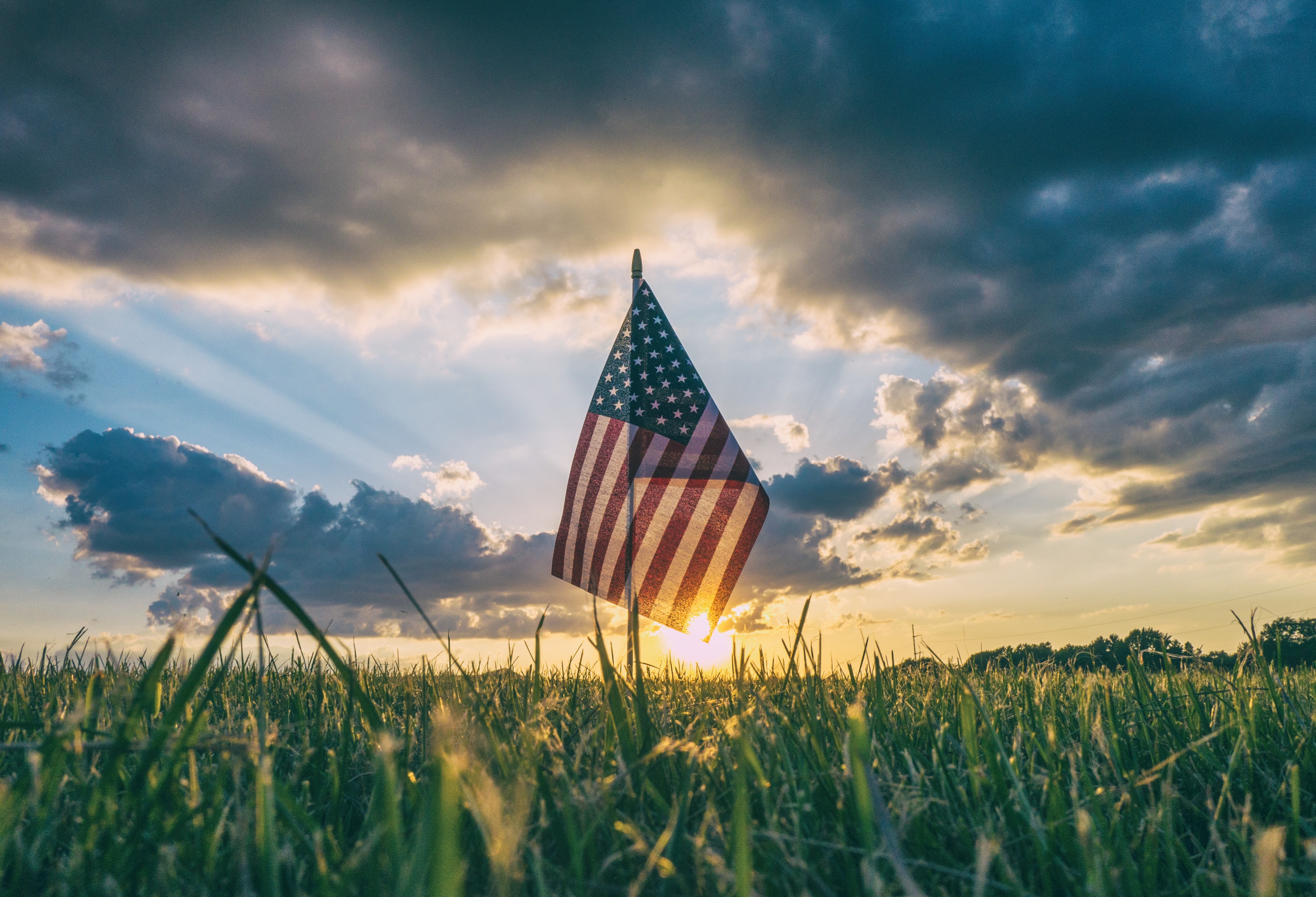 American Flag planted in green grass overlooking partially cloudy sky and golden sunset