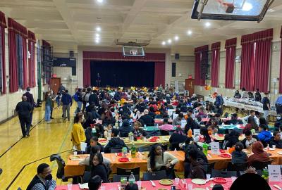 Gymnasium set up for Thanksgiving potluck with students seated at tables with their CORE leaders